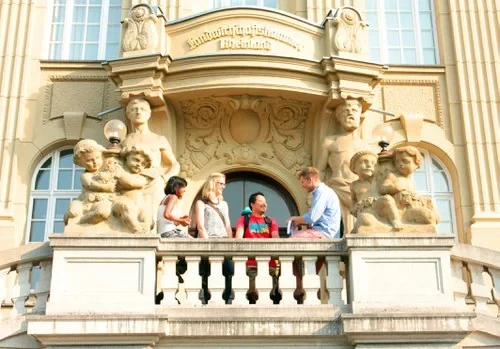 Eine Wissenschaftlerin und ein Wissenschaftler arbeiten hinter einer Glasfassade und mischen Chemikalien mit Großgeräten.